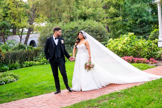 Bride and groom walking a garden path, veil trailing behind.