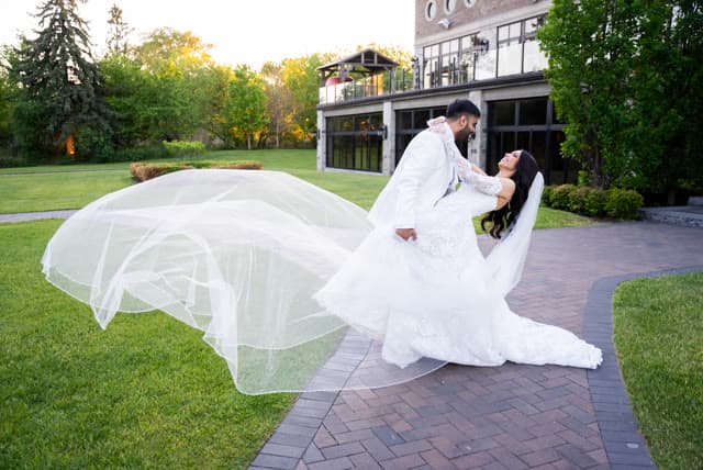 Bride and groom dip and kiss, veil catching the wind.