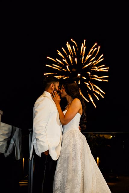 Bride and groom, close portrait, fireworks behind them.
